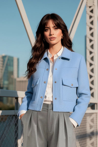 Chamarra corta de fit recto, cuello camisero, manga larga con puño abotonado, cortes decorativos frontales, bolsillos delanteros con cartera y botón. Cierre frontal con hilera de botones en contraste.