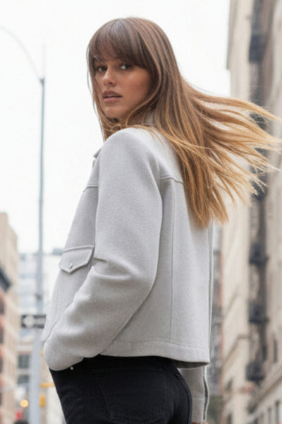 Chamarra corta de fit recto, cuello camisero, manga larga con puño abotonado, cortes decorativos frontales, bolsillos delanteros con cartera y botón. Cierre frontal con hilera de botones en contraste.