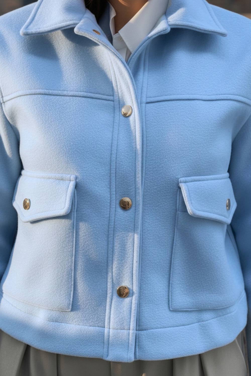 Chamarra corta de fit recto, cuello camisero, manga larga con puño abotonado, cortes decorativos frontales, bolsillos delanteros con cartera y botón. Cierre frontal con hilera de botones en contraste.