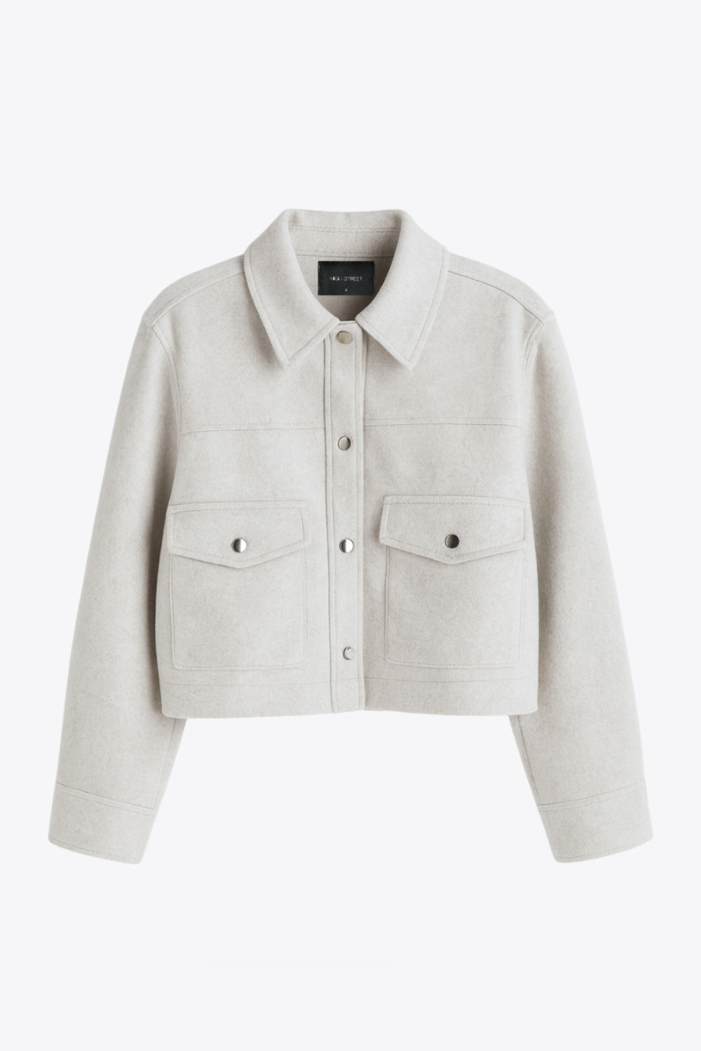 Chamarra corta de fit recto, cuello camisero, manga larga con puño abotonado, cortes decorativos frontales, bolsillos delanteros con cartera y botón. Cierre frontal con hilera de botones en contraste.