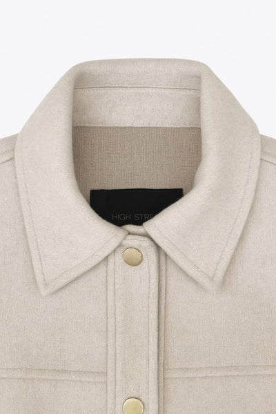 Chamarra corta de fit recto, cuello camisero, manga larga con puño abotonado, cortes decorativos frontales, bolsillos delanteros con cartera y botón. Cierre frontal con hilera de botones en contraste.