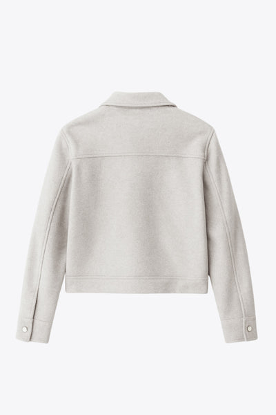 Chamarra corta de fit recto, cuello camisero, manga larga con puño abotonado, cortes decorativos frontales, bolsillos delanteros con cartera y botón. Cierre frontal con hilera de botones en contraste.