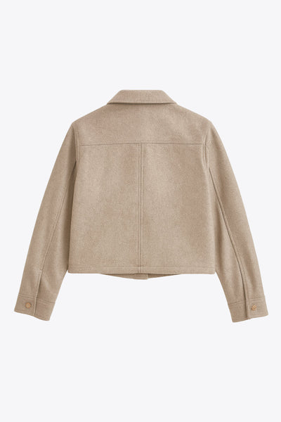 Chamarra corta de fit recto, cuello camisero, manga larga con puño abotonado, bolsillos delanteros con cartera y botón. Cierre frontal con hilera de botones en contraste.