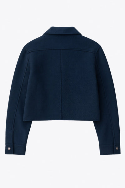 Chamarra corta de fit recto, cuello camisero, manga larga con puño abotonado, bolsillos delanteros con cartera y botón. Cierre frontal con hilera de botones en contraste.