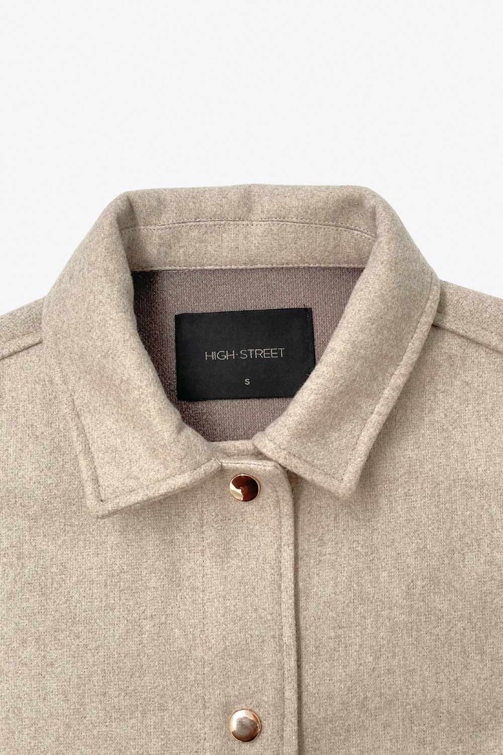 Chamarra corta de fit recto, cuello camisero, manga larga con puño abotonado, bolsillos delanteros con cartera y botón. Cierre frontal con hilera de botones en contraste.