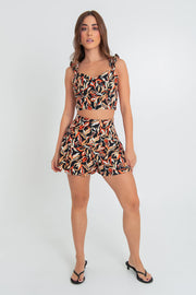 Crop top de estampado abstracto, fit ajustado, escote corazón con cortes decorativos, costuras frontales y tirantes fruncidos con olanes. Cierre posterior con cremallera visible en contraste.