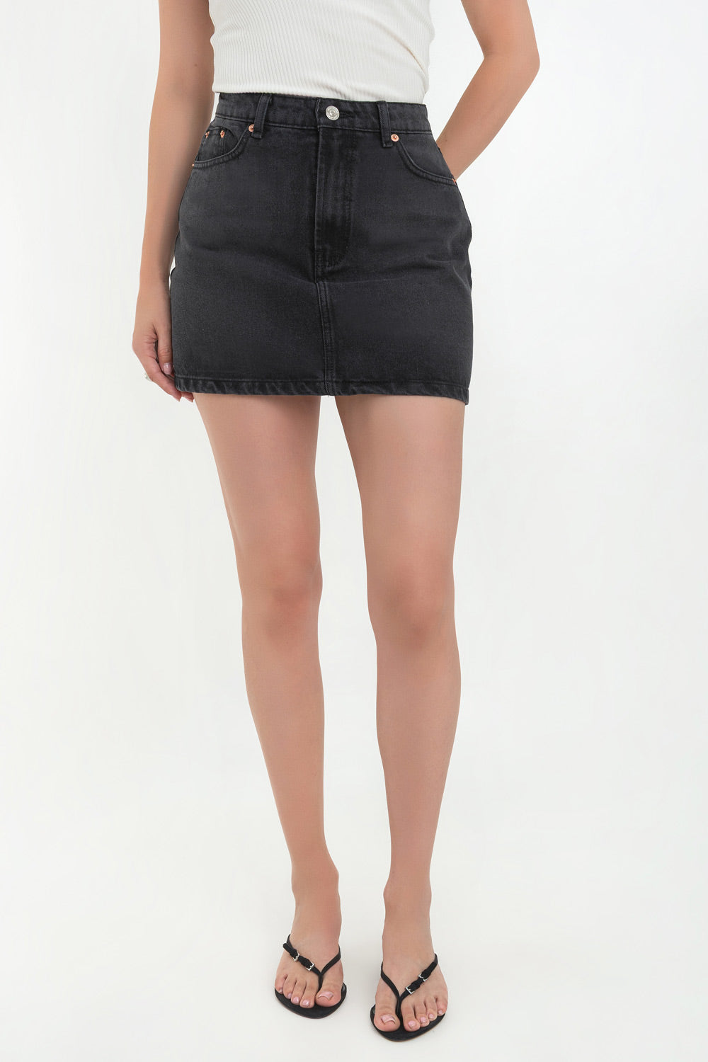 Falda corta básica de denim, fit ajustado, cintura alta con pretina y trabillas, bolsillos delanteros y traseros de parche. Cierre frontal con botón y cremallera oculta.