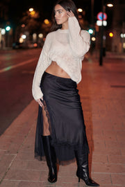 Falda midi satinada de corte en a, cintura alta, bajo asimétrico con encaje en borde y abertura frontal. Cierre lateral con cremallera oculta.