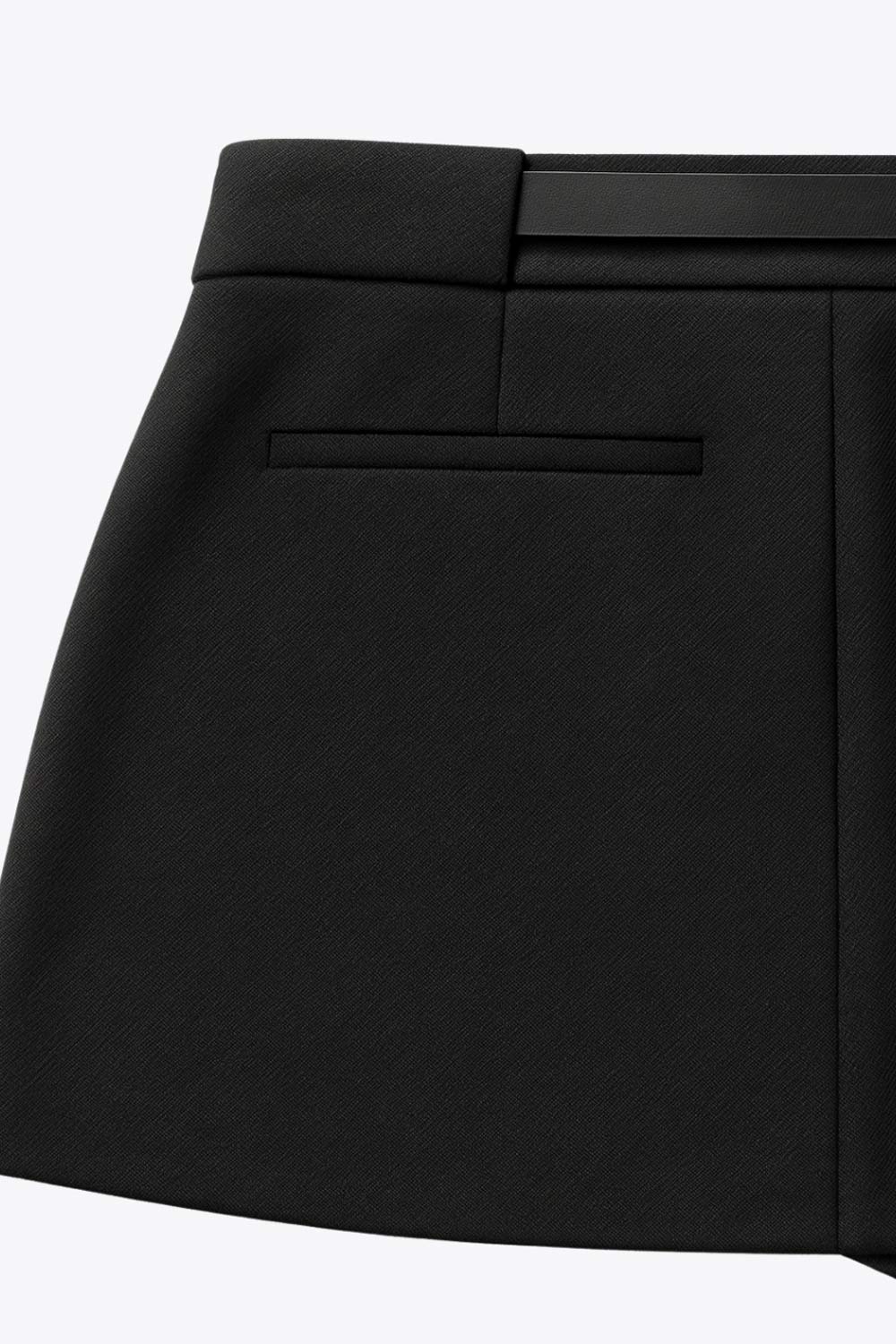 Falda short corto de fit recto, cintura alta con pretina y trabillas, vivos decorativos posteriores, cierre frontal con broche y cremallera ocultos. Detalle de cinturón en contraste con hebilla.