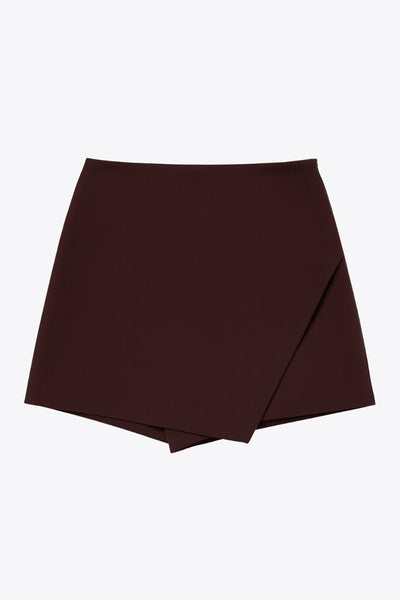 Falda short de fit ajustado, cintura alta, cruce frontal asimétrico, vivos decorativos posteriores y cierre lateral con cremallera oculta.