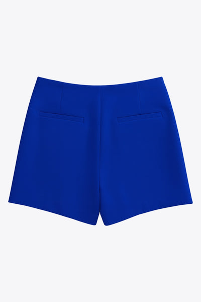 Falda short corto de fit ajustado, cintura alta, cruce frontal con nudo y plisados decorativos frontales. Cierre posterior con cremallera oculta.