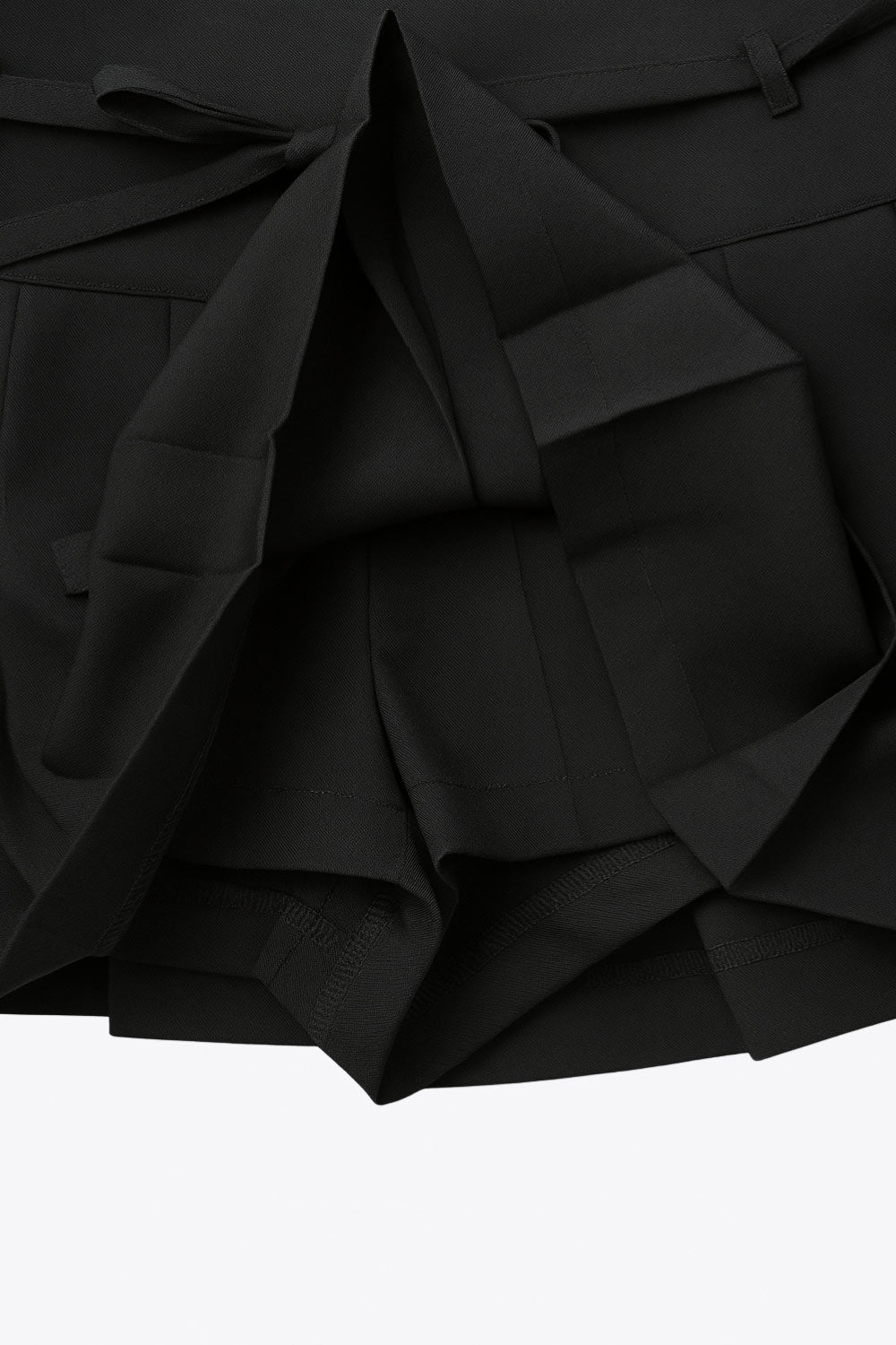 Falda short corto tableado, de corte en a, cintura alta con pretina, trabillas y lazo amarrable del tejido. Detalle de tableado en bajo y cierre lateral con cremallera oculta.