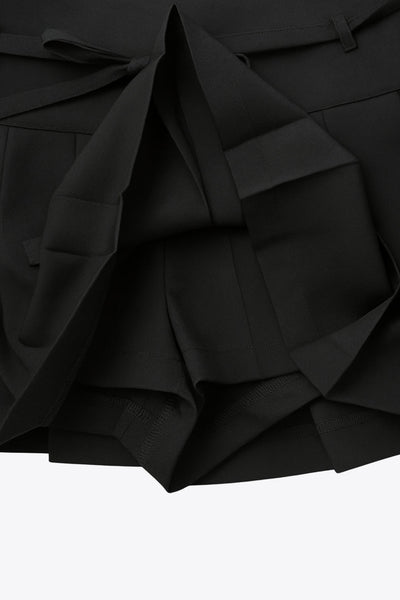 Falda short corto tableado, de corte en a, cintura alta con pretina, trabillas y lazo amarrable del tejido. Detalle de tableado en bajo y cierre lateral con cremallera oculta.