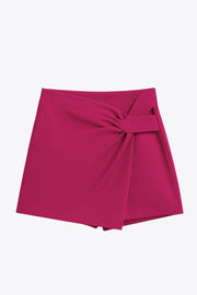 Falda short corto de fit ajustado, cintura alta, cruce frontal con nudo y plisados decorativos frontales. Cierre posterior con cremallera oculta.