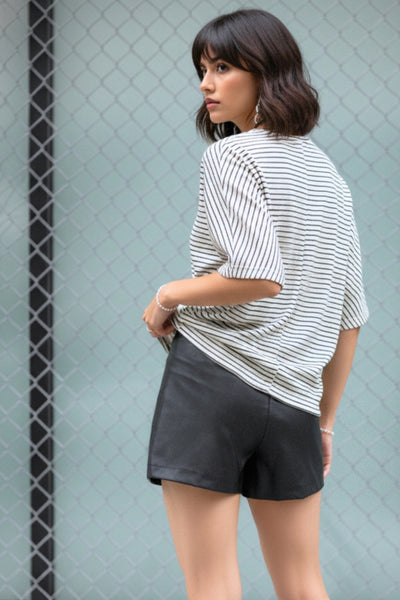 Falda short corto de efecto piel, fit ajustado, cintura alta, cruce frontal asimétrico con nudo y plisados decorativos frontales. Cierre posterior con cremallera oculta.