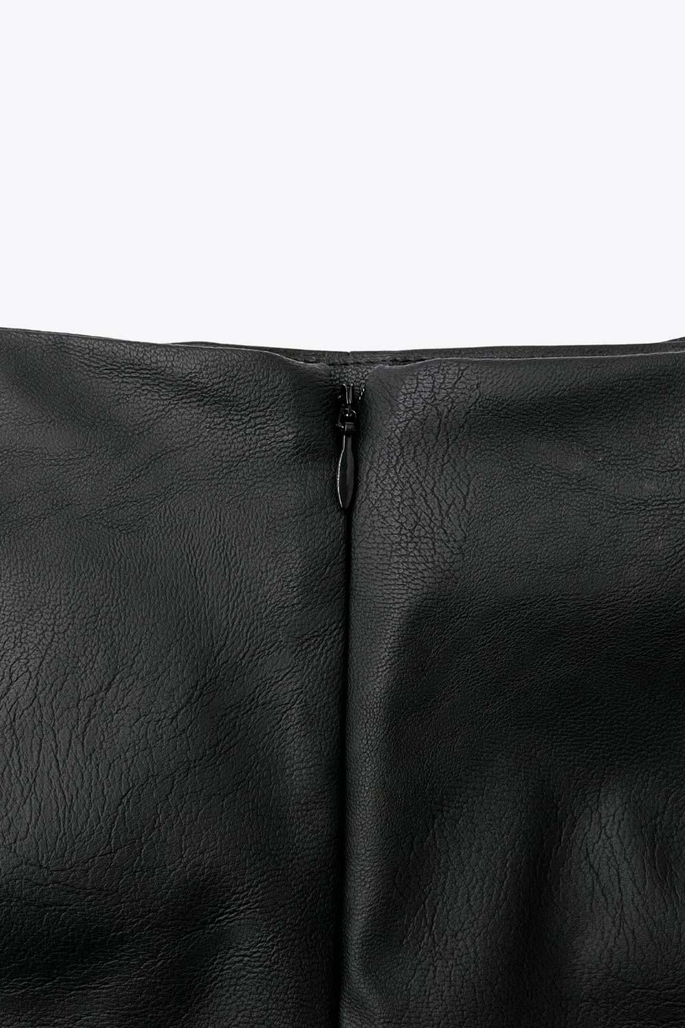 Falda short corto de efecto piel, fit ajustado, cintura alta, cruce frontal asimétrico con nudo y plisados decorativos frontales. Cierre posterior con cremallera oculta.