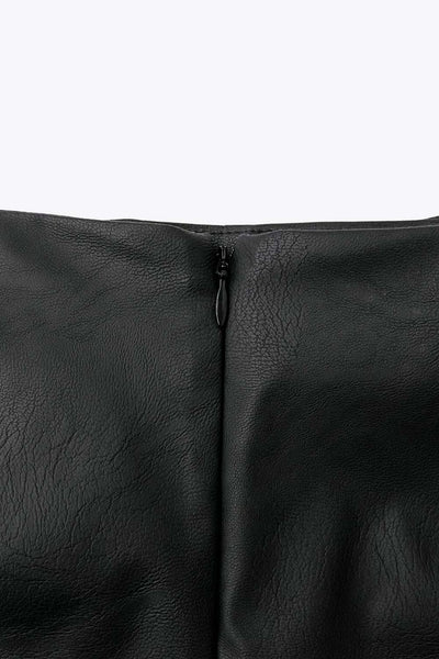 Falda short corto de efecto piel, fit ajustado, cintura alta, cruce frontal asimétrico con nudo y plisados decorativos frontales. Cierre posterior con cremallera oculta.