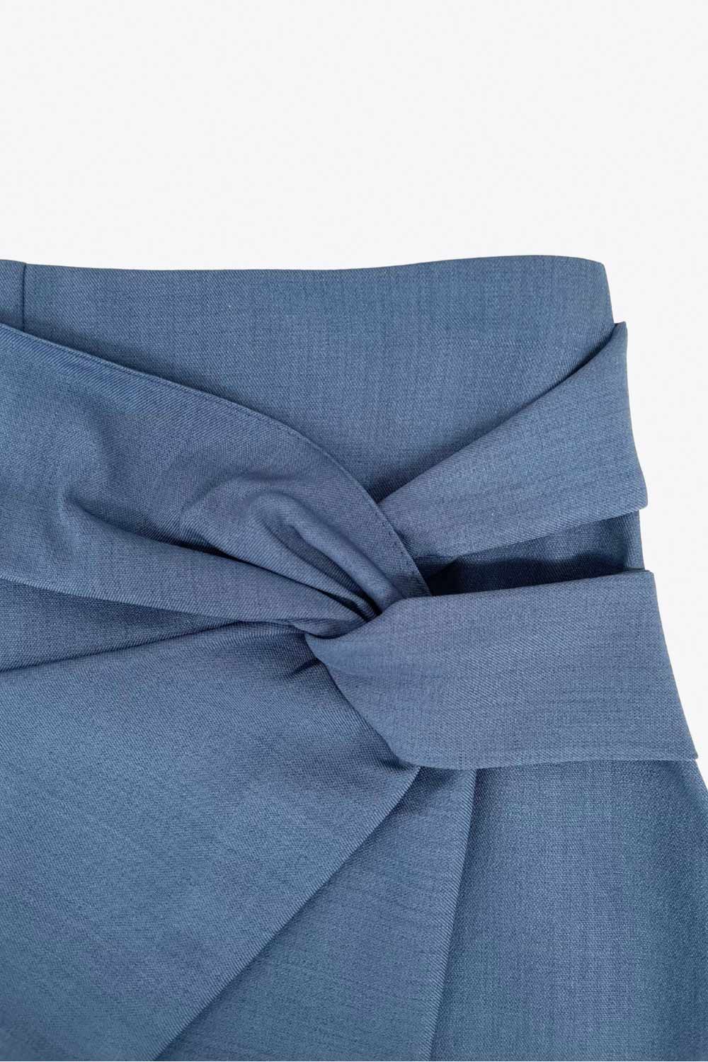 Falda short corto de fit ajustado, cintura alta, cruce frontal con nudo y plisados decorativos frontales. Cierre posterior con cremallera oculta.