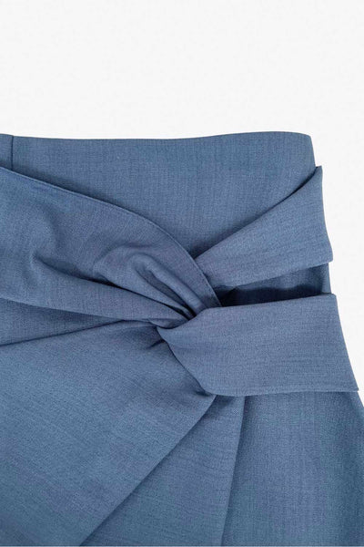 Falda short corto de fit ajustado, cintura alta, cruce frontal con nudo y plisados decorativos frontales. Cierre posterior con cremallera oculta.