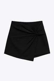 Falda short corto de fit ajustado, cintura alta, cruce frontal con nudo y plisados decorativos frontales. Cierre posterior con cremallera oculta.