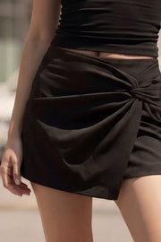 Falda short corto de fit ajustado, cintura alta, cruce frontal con nudo y plisados decorativos frontales. Cierre posterior con cremallera oculta.