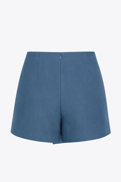 Falda short corto de fit ajustado, cintura alta, cruce frontal con nudo y plisados decorativos frontales. Cierre posterior con cremallera oculta.