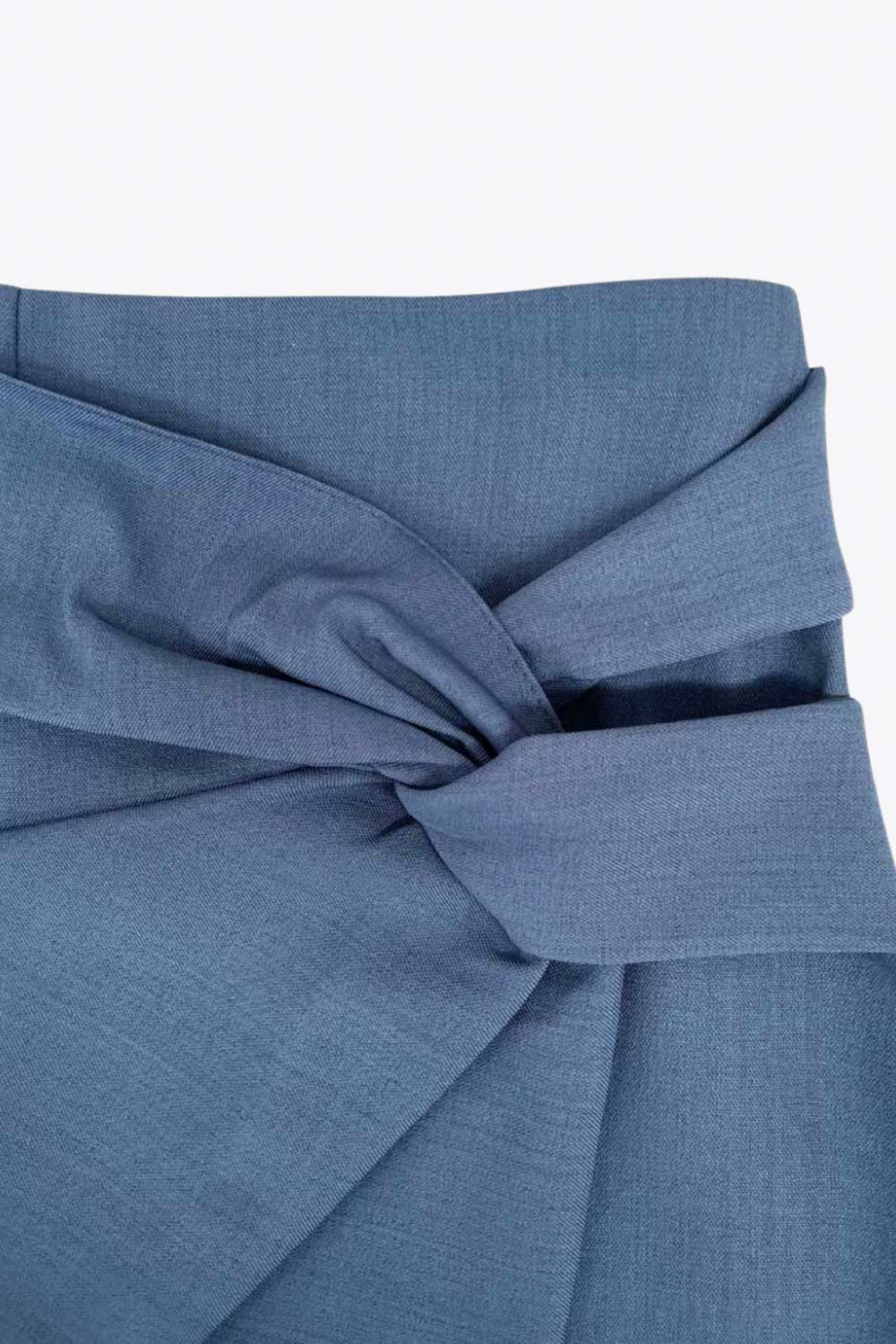 Falda short corto de fit ajustado, cintura alta, cruce frontal con nudo y plisados decorativos frontales. Cierre posterior con cremallera oculta.