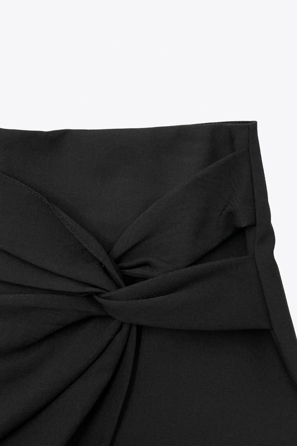 Falda short corto de fit ajustado, cintura alta, cruce frontal con nudo y plisados decorativos frontales. Cierre posterior con cremallera oculta.