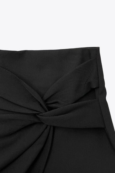 Falda short corto de fit ajustado, cintura alta, cruce frontal con nudo y plisados decorativos frontales. Cierre posterior con cremallera oculta.