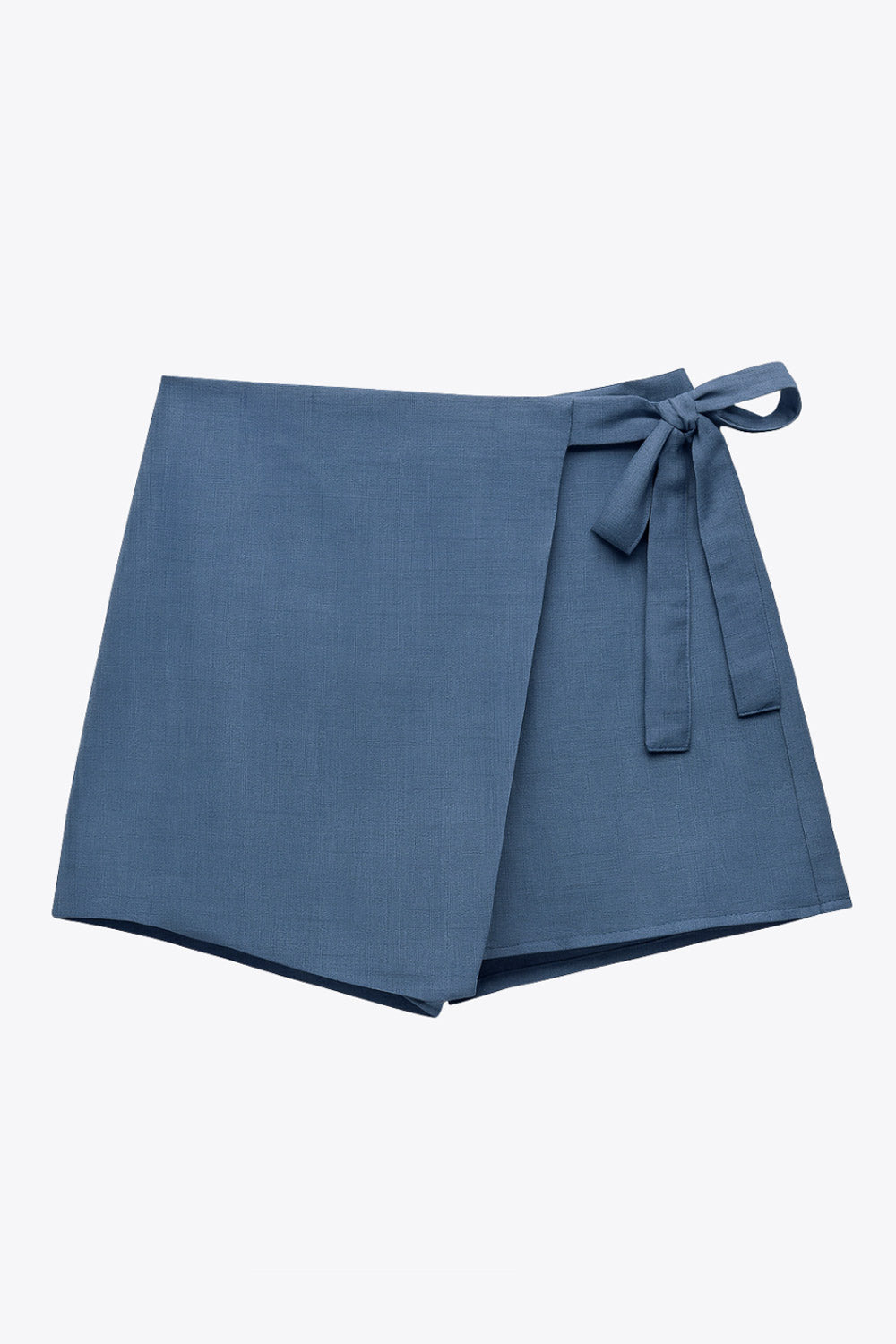 Falda short corto de cintura alta, corte en a, sobrefalda con cruce frontal, lazo lateral amarrable y cierre posterior con cremallera oculta.