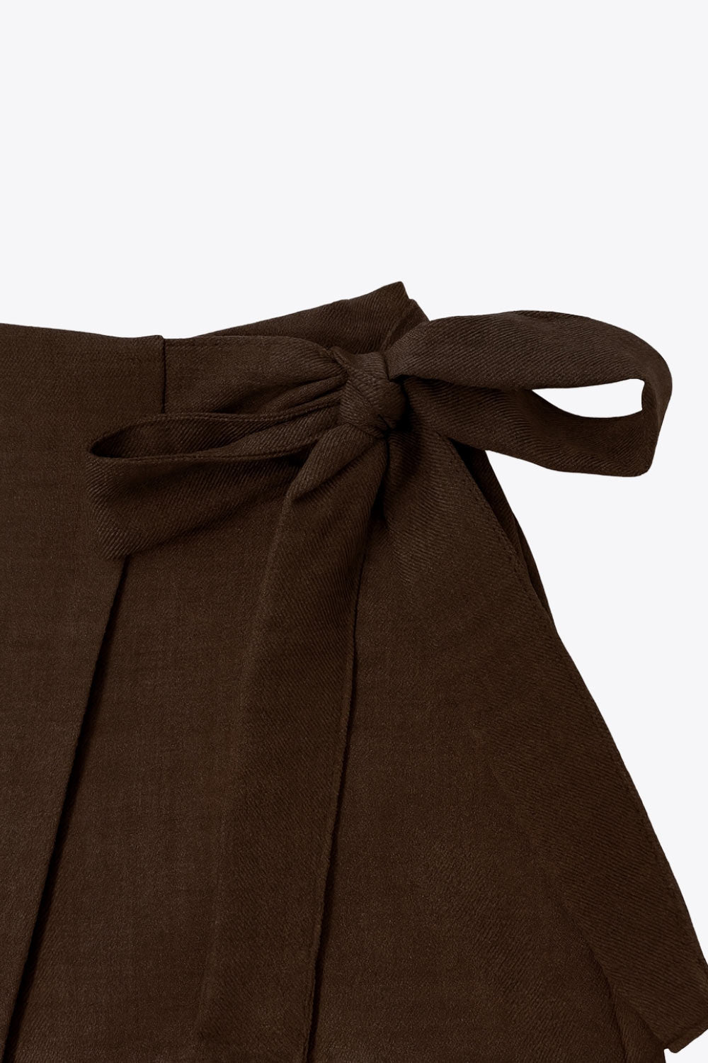 Falda short corto de cintura alta, corte en a, sobrefalda con cruce frontal, lazo lateral amarrable y cierre posterior con cremallera oculta.