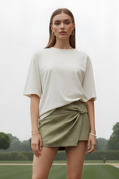 Falda short de fit ajustado, cintura alta, nudo frontal con plisados decorativos y bajo asimétrico. Cierre posterior con cremallera oculta.