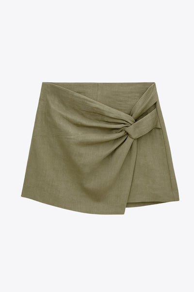 Falda short de fit ajustado, cintura alta, nudo frontal con plisados decorativos y bajo asimétrico. Cierre posterior con cremallera oculta.