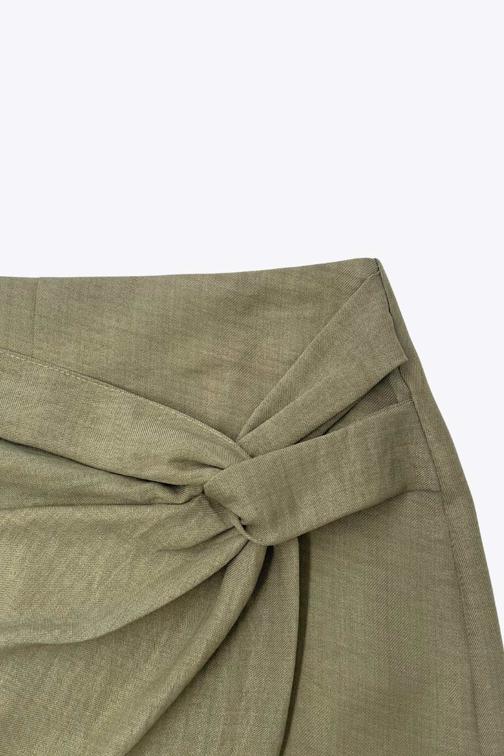 Falda short de fit ajustado, cintura alta, nudo frontal con plisados decorativos y bajo asimétrico. Cierre posterior con cremallera oculta.