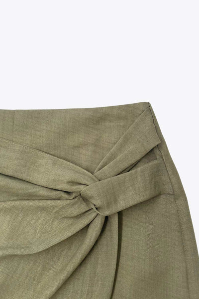 Falda short de fit ajustado, cintura alta, nudo frontal con plisados decorativos y bajo asimétrico. Cierre posterior con cremallera oculta.