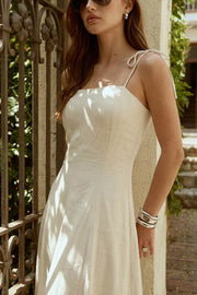 Vestido largo de fit ajustado, corte en a con olanes en bajo, tirantes delgados con nudo amarrable, escote recto y cierre posterior con cremallera oculta.