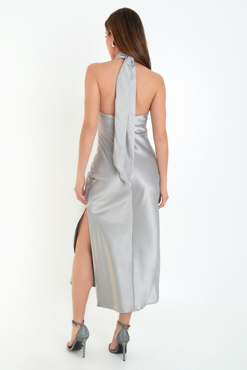 Maxi vestido satinado de fit recto, cuello halter cruzado con lazo amarrable posterior, escote en espalda y cierre posterior con cremallera oculta. Detalle de abertura lateral en bajo.