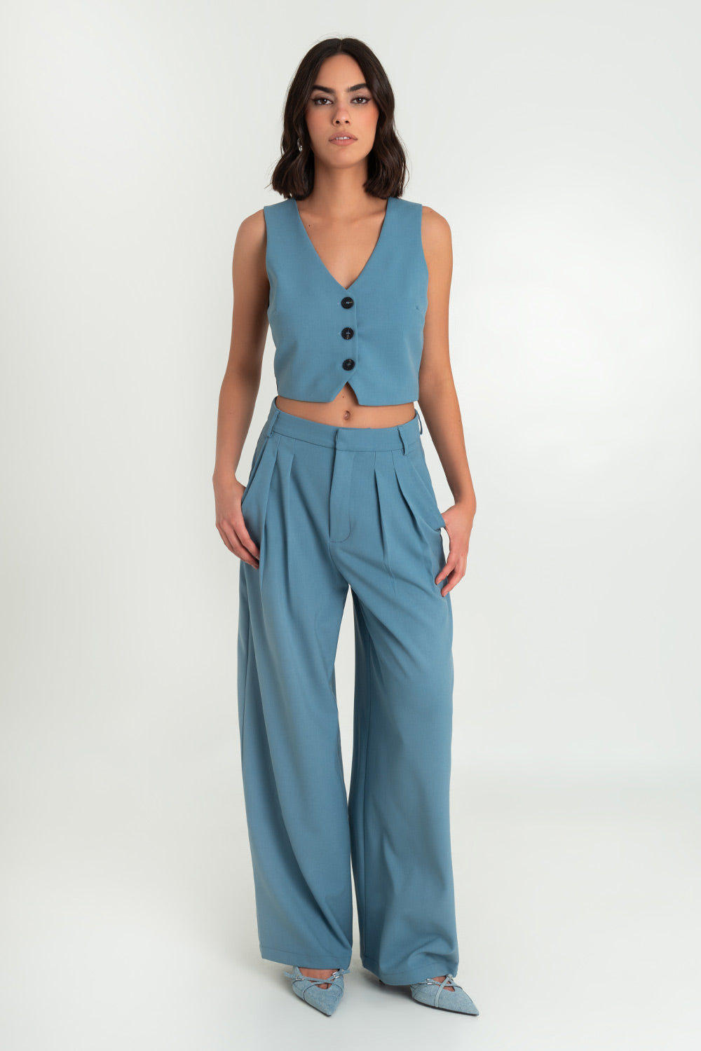 Pantalón de fit wide leg, cintura alta con pretina y trabillas, bolsillos delanteros y pinzas frontales. Cierre frontal con broche y cremallera oculta.