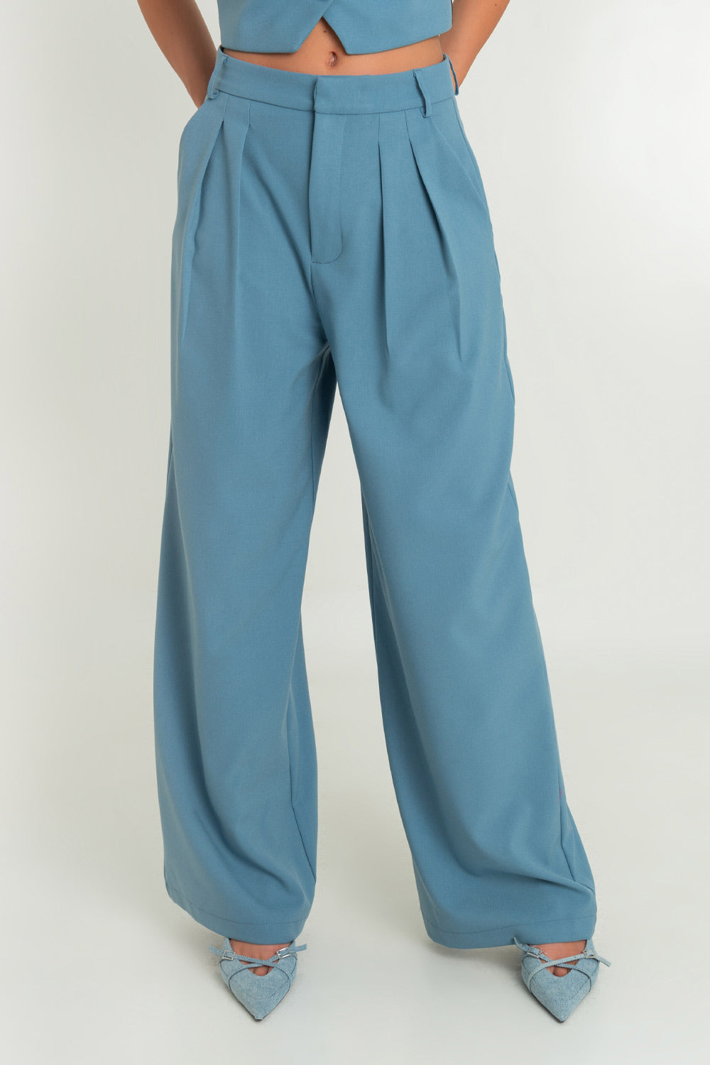Pantalón de fit wide leg, cintura alta con pretina y trabillas, bolsillos delanteros y pinzas frontales. Cierre frontal con broche y cremallera oculta.