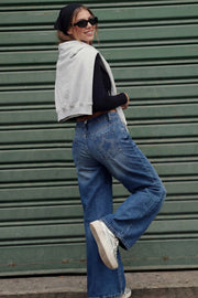 Pantalón wide leg de denim, cintura media con pretina y trabillas, bolsillos delanteros y traseros de parche con bordado de estrella. Cierre frontal con botón y cremallera oculta.
