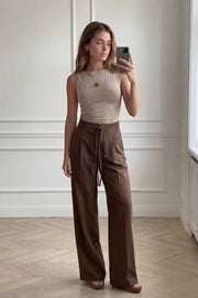 Pantalón de fit wide leg, cintura alta con pretina, trabillas y doble lazo amarrable, pinzas frontales y bolsillos delanteros. Cierre frontal con broche y cremallera ocultos.