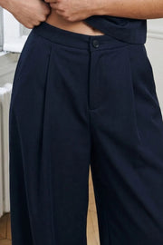 Pantalón fit barrel de cintura media con pretina elástica posterior, bolsillos delanteros, pinzas frontales y rib elástico en bajo. Cierre frontal con botón y cremallera oculta.