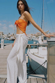 Pantalón fluido de fit palazzo, cintura media con pretina elástica, plisados en costado y detalle de pareo decorativo con nudo lateral.