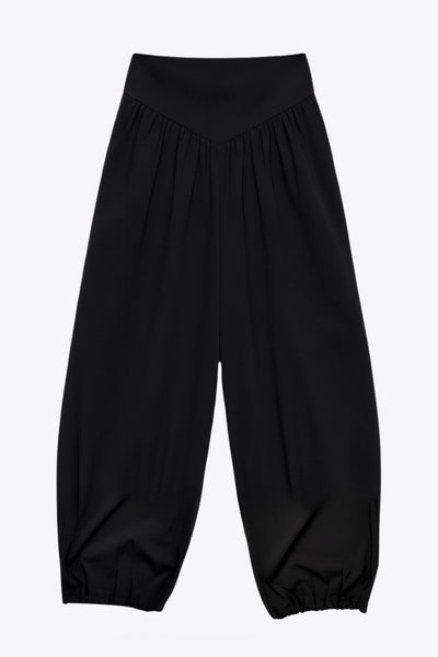 Pantalón de fit harem, cintura alta, peto con corte v frontal y plisado decorativos, rib elástico en bajo y cierre lateral con cremallera oculta.