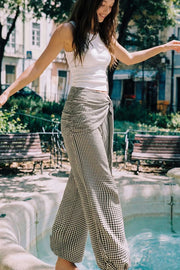 Pantalón fluido de fit palazzo, estampado cuadros, cintura media con pretina elástica, plisados en costado y detalle de pareo decorativo con nudo lateral.