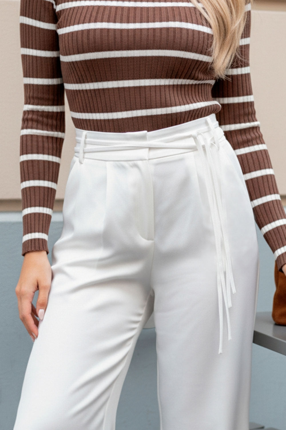 Pantalón de fit wide leg, cintura alta con pretina, trabillas y doble lazo amarrable, pinzas frontales y bolsillos delanteros. Cierre frontal con broche y cremallera ocultos.