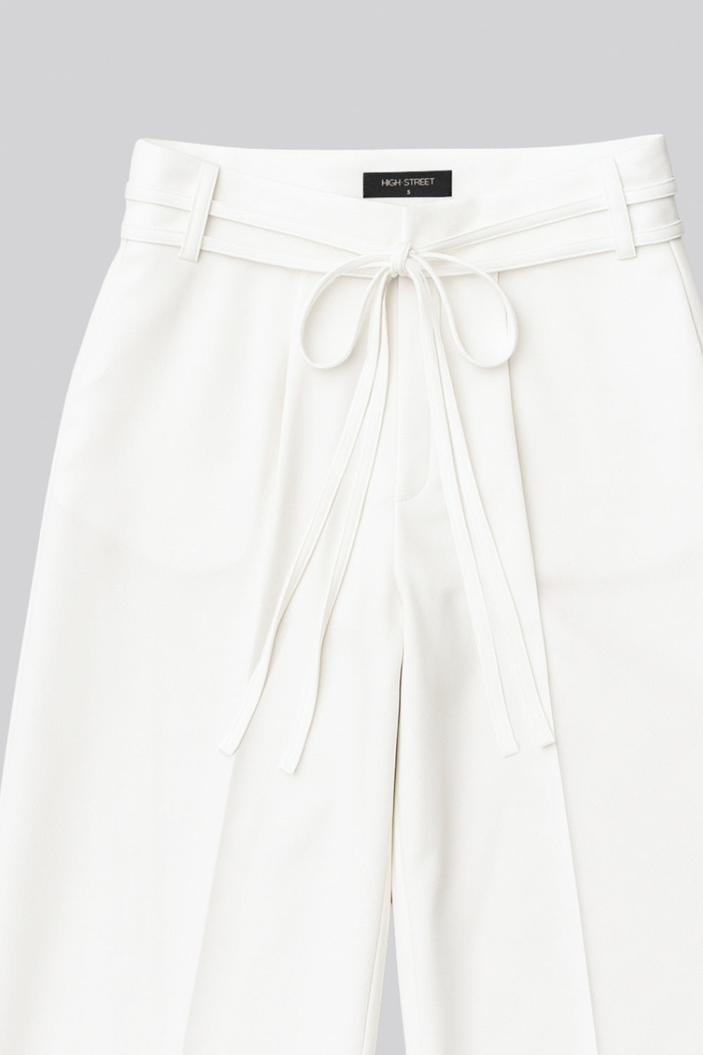 Pantalón de fit wide leg, cintura alta con pretina, trabillas y doble lazo amarrable, pinzas frontales y bolsillos delanteros. Cierre frontal con broche y cremallera ocultos.