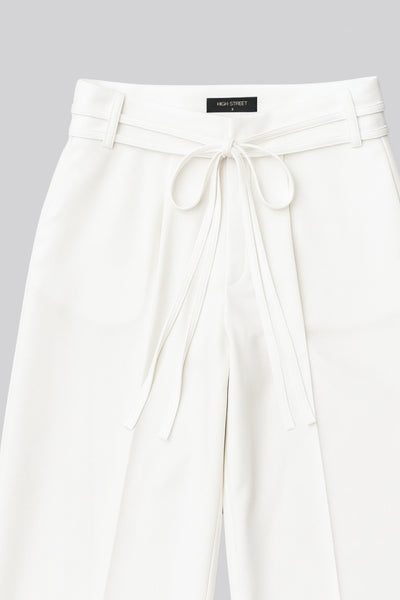 Pantalón de fit wide leg, cintura alta con pretina, trabillas y doble lazo amarrable, pinzas frontales y bolsillos delanteros. Cierre frontal con broche y cremallera ocultos.