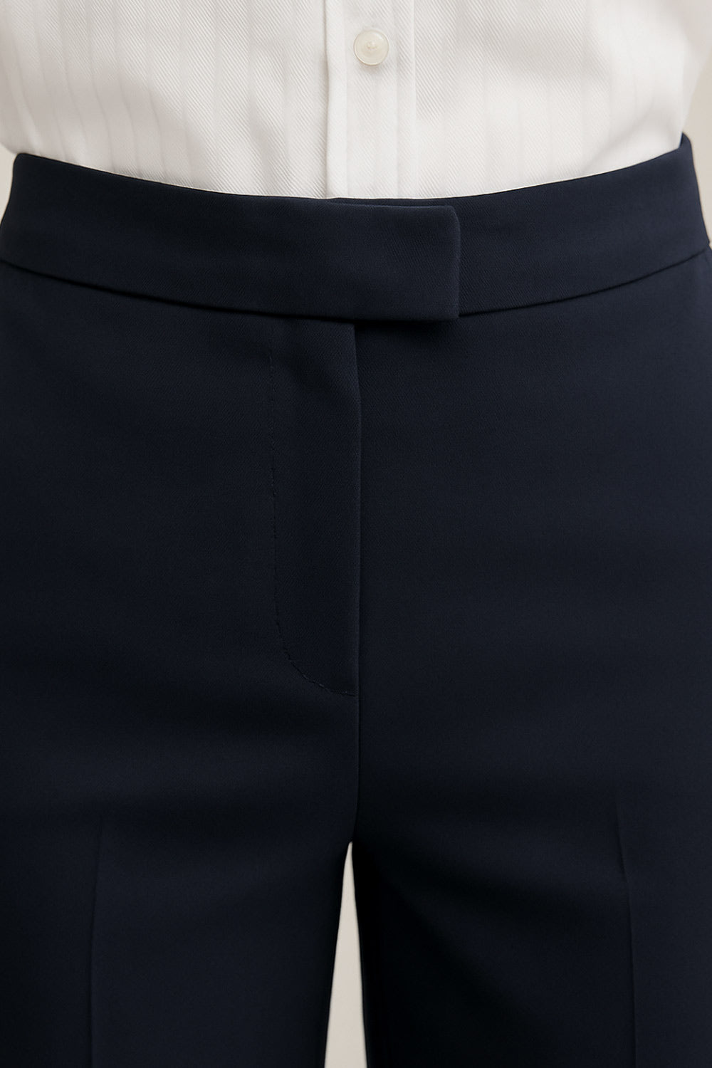 Pantalón ajustado de fit flare, cintura media con pretina, bolsillos delanteros y vivos decorativos posteriores. Cierre frontal con broche y cremallera ocultos.