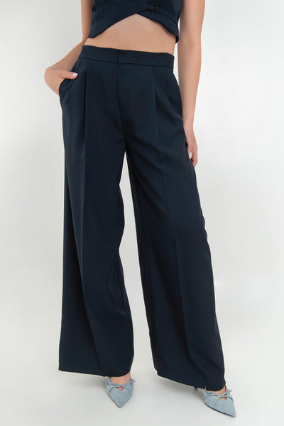 Pantalón de fit wide leg, cintura alta con pretina, pinzas frontales, bolsillos delanteros y vivos decorativos posteriores. Cierre frontal con broche y cremallera ocultos. Detalle v en pretina posterior.